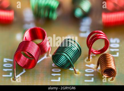 Electronic air-core inductors on beige printed circuit board detail. Closeup of colored spiral copper wire windings of coils inside TV receiver part. Stock Photo