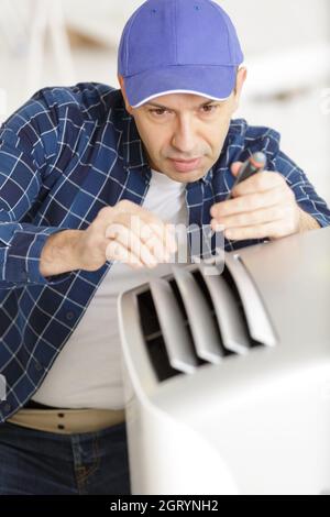 mature male technician fixing air conditioner with screwdriver Stock Photo