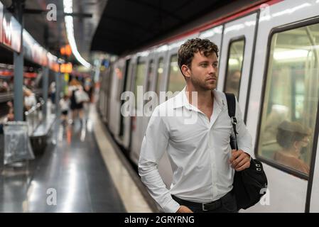 Businessman with bag walking near modern train on platform of subway station while commuting to work Stock Photo