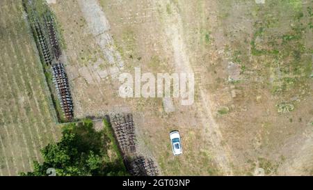 High aspect top down view of a white car with sunroof parked beside old discarded railway tracks with trees beyond the fence Stock Photo