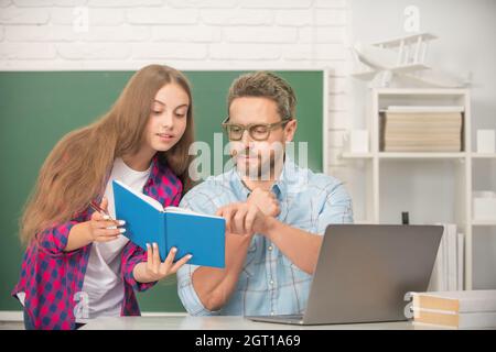 attentive teen girl and teacher man in high school with workbook and pc at blackboard, schoolwork Stock Photo