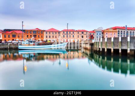 Hobart city harbour waterfront of historic colourful buildings with fishing yacht at sunset reflecting in still waters. Stock Photo