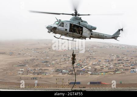 A U.S. Marine with Special Purpose Marine Air-Ground Task Force – UNITAS, descends a rope from a UH-1Y Venom helicopter during a fast-rope training evolution at Peruvian Marine Corps Base Ancon, Peru, Sept. 26, 2021, during exercise UNITAS LXII. U.S., Brazilian, Chilean, Colombian, Mexican, and Peruvian Marines and members of the Jamaican Defense Force completed a series of training events in order to build trust, enhance confidence and strengthen interoperability to better prepare us for a combined, multinational response to emerging crises or natural disasters. UNITAS is the world's longest- Stock Photo