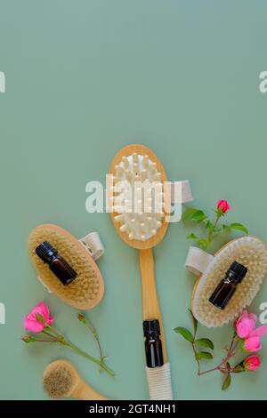 Rose oil. Spa, massage and aromatherapy. Massage brushes set, oil in glass bottles and rose flowers on a green background.  Stock Photo