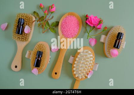 Rose essential oil. Spa, massage and aromatherapy. Massage brushes set, oil in glass bottles and pink rose flowers on a green background.  Stock Photo
