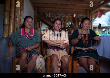 Nueva Loja, Sucumbios / Ecuador - September 2 2020: Indigenous woman of Cofan nationality with green dress smiling while weaving handicrafts sitting o Stock Photo