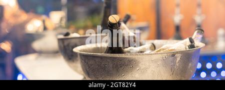 Wine in glass bottles is cooled in a metal bucket. Tasting of alcoholic beverages at the exhibition of winemakers. Foreground. Stock Photo