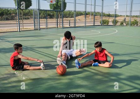 Basketball coach doing leg stretching exercises with two children. Stock Photo