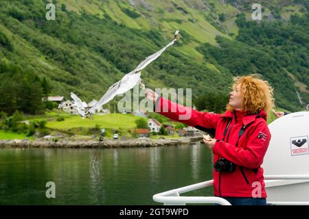 SOGNEFJORD, NORWAY - JULY 3, 2016: Unknown woman feeds gulls away with the ferry deck, floating on the fjord. Stock Photo