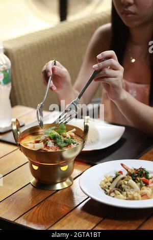 Midsection Of Woman Eating Thai Food. Tom Yum Soup. Hand Woman's Hold Spoon And Fork.