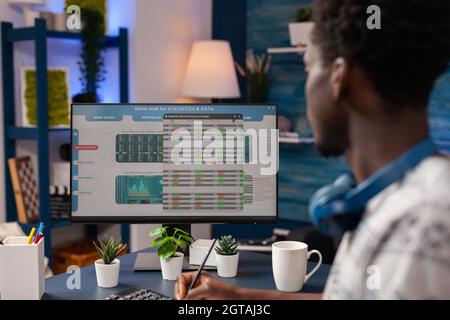 African american trader writing crypto currency earning on notebook analyzing global investment. Young broker working remote from home with stock market charts checking trading value Stock Photo