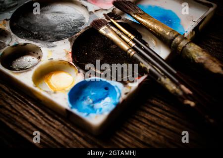 Color brushes and color mixed in white palette on wooden table Stock Photo