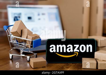 Smartphone with Amazon logo on the screen, shopping cart and laptop. Stock Photo