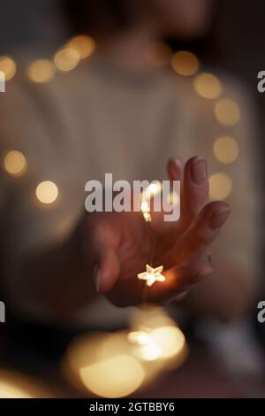 Woman holds a glowing star in her hand to make a wish. Lady hand hold Christmas decoration with bokeh lights