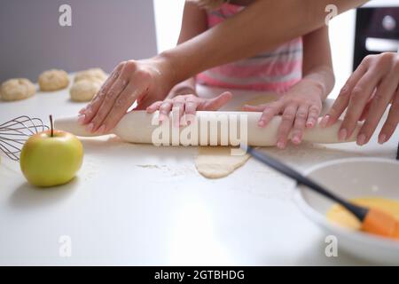 Mom and daughter roll out dough with rolling pin in kitchen Stock Photo