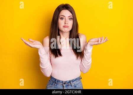 Photo of unsure brunette lady shrug shoulders wear pink shirt isolated on yellow color background Stock Photo