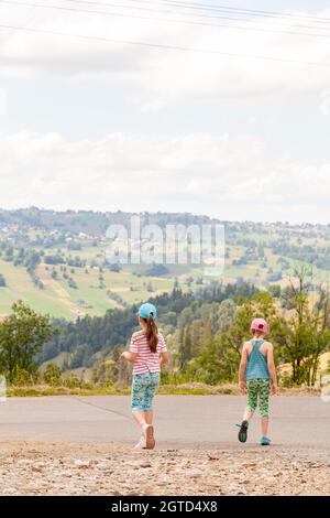 Two young elementary age children traveling, little girls, sisters exploring together, walking down the road, hills, scenic mountain rural area, count Stock Photo