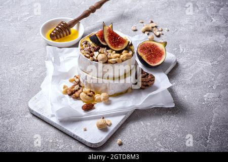 Gourmet appetizer of white brie cheese or camembert with fresh figs, nuts and honey on grey concrete background Stock Photo