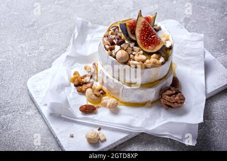 Gourmet appetizer of white brie cheese or camembert with fresh figs, nuts and honey on grey concrete background Stock Photo