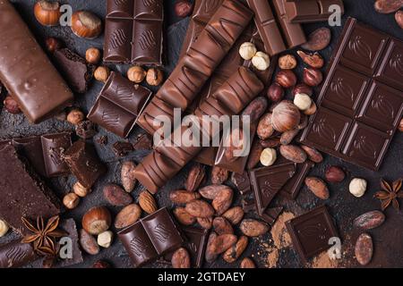Pieces of broken tasty milk and dark chocolate bars with cocoa beans and hazelnut on brown concrete background Stock Photo
