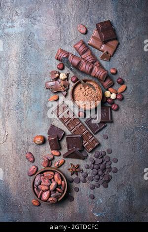 Pieces of broken tasty milk and dark chocolate bars with drops, cocoa beans and hazelnut on blue concrete background Stock Photo