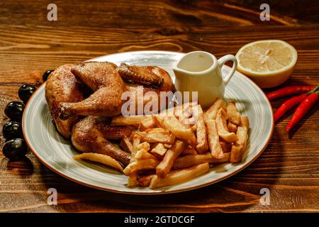Grilled chicken legs with french fries, chips in plate with lemons and olives Stock Photo