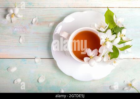 White Cup Of Tea With Blossoming Apple Tree Flowers On Shaped Saucer On Painted Wooden Table.