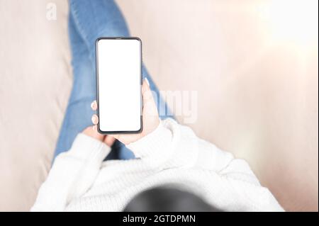 cell phone blank white screen mockup. woman hand holding texting using mobile on sofa at home.background empty space for advertise. winter time top vi Stock Photo