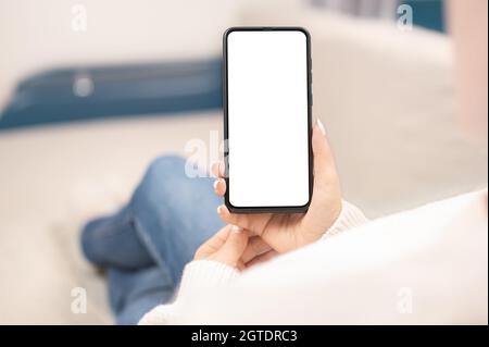 working at home using with smart cell phone. Woman using smartphone frameless mockup blank screen in home interior. Woman using mobile phone with empt Stock Photo