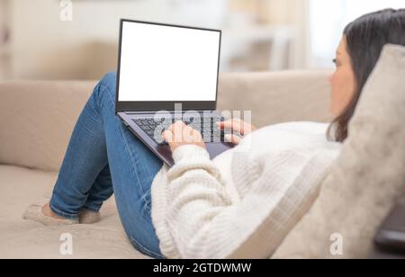Mockup laptop. Close up of female sit on cozy sofa typing on laptop, woman freelancer working at computer from home. Laptop computer blank white scree Stock Photo