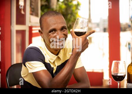 handsome young man holding a glass of red wine and looking at the camera while smiling Stock Photo