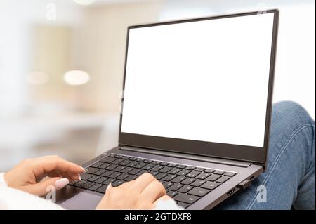 laptop mockup with blank white screen, woman holds laptop on her knees lying on sofa at home. woman sits on her lap with laptop in a bright room. wome Stock Photo