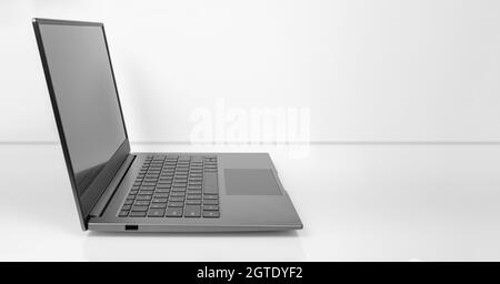 Laptop on a light table. black screen with reflections, gray metal aluminum material body, side view. copy space, wide image Stock Photo