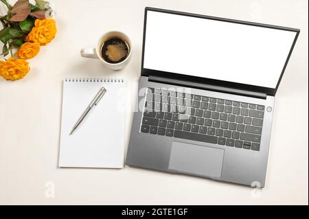 Mockup computer laptop with white blank screen coffee , flower, notepad and pen on work office desk, Top view office desk. Office desktop. Stock Photo