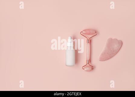 Composition of white mockup serum bottle, pink quarts stone face roller and gua sha stone on pink background. Natural cosmetics concept. Creative cosmetics flat lay with copy space. Stock Photo