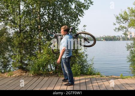 frustrated man in the park carries broken bicycle on his shoulder. Stock Photo