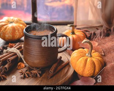 Steaming mug of hot chocolate and mini pumpkins by a window with colorful autumn background Stock Photo