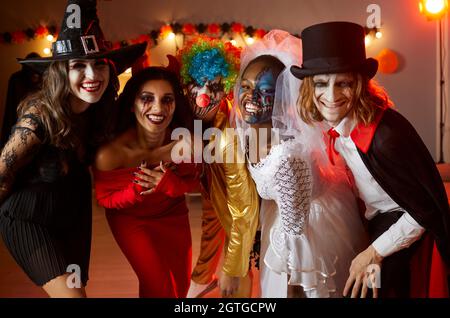 Group of happy friends dressed up in spooky Halloween costumes standing together and smiling Stock Photo