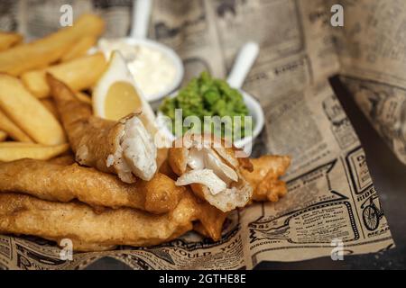 British Traditional crispy Fish and chips with mashed peas, tartar sauce on newspaper Stock Photo