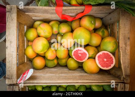 Wooden box with organic fresh grapefruit, a few cut open on a outdoor fruit market. Stock Photo