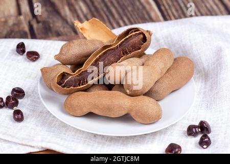 Fresh brown tamarind fruit pods ripe with seeds on light textile background close up. Stock Photo