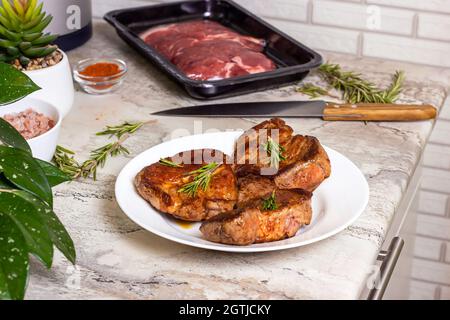 Fresh prepared roasted beef steak with spices and rosemary on white round plate on the kitchen table background. Stock Photo