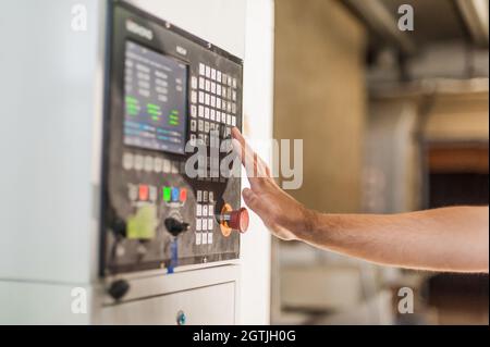 Close-up detail view of professional worker technician machinist pressing emergency stop button on control panel in factory production workplace. Indu Stock Photo