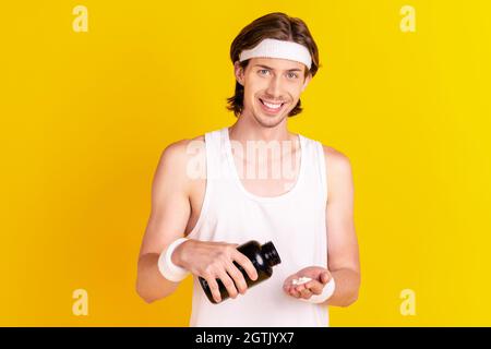 Portrait of attractive cheerful guy taking sportive organic pills isolated over bright yellow color background Stock Photo