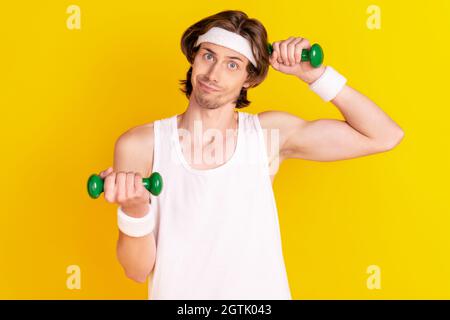 Portrait of attractive weak clueless sportive guy lifting weight isolated over bright yellow color background Stock Photo