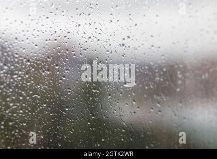 Rainy day through the window on cloudy grey sky and city buildings background. Concept. Evening cityscape behind the glass window with trickling drops Stock Photo