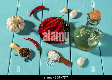 Spices on a rustic turquoise wooden table. Raw red hot chili peppers, head and cloves of garlic, sea salt and black peppercorns in wooden spoons. Stock Photo
