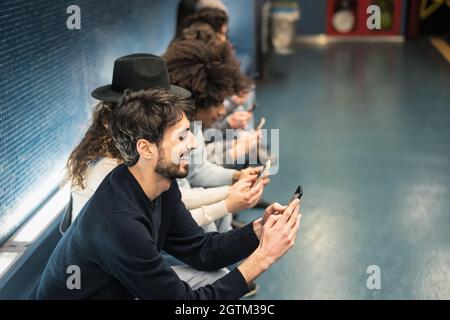 Young people using mobile smartphone while sitting in subway station waiting train - Youth millennial addicted to new technology concept Stock Photo