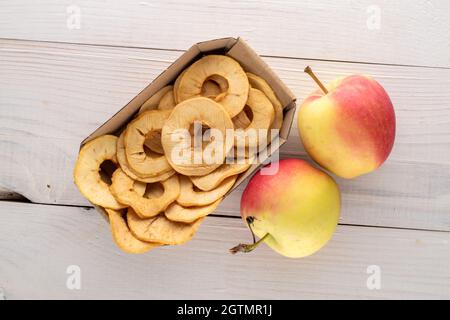 Several crispy apple chips in a paper dish and two apples on a wooden table, close-up, top view. Stock Photo
