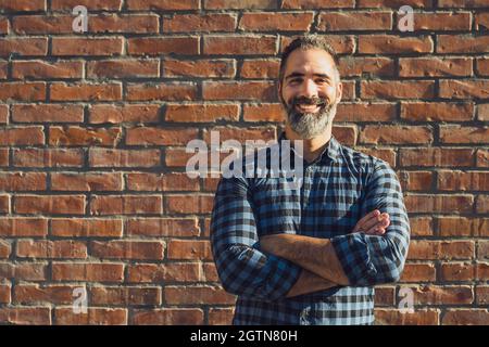 Portrait of modern businessman with beard standing in front of brick wall outdoor. Stock Photo